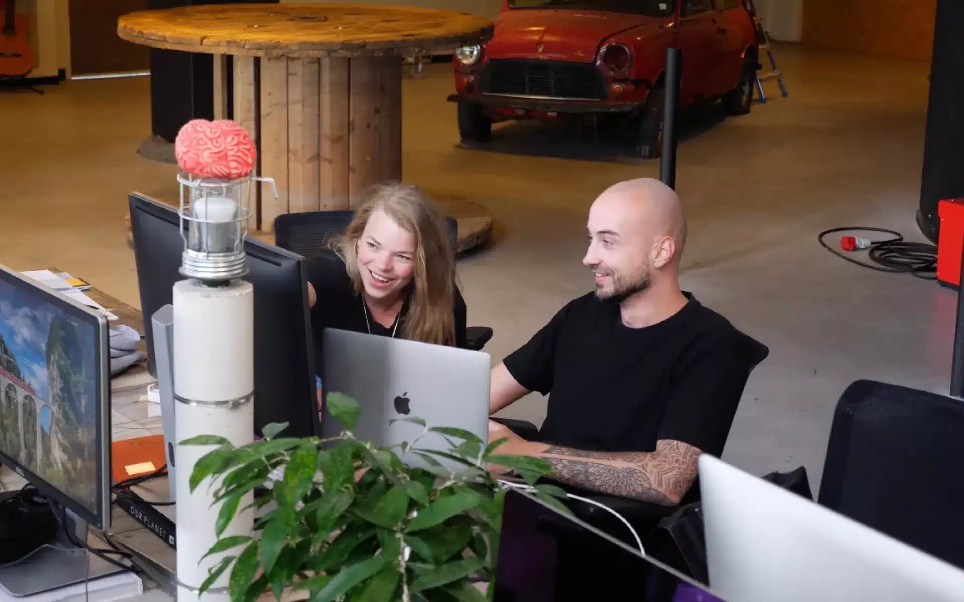 Twee collega’s van All You Can Learn werken samen achter hun computerschermen.