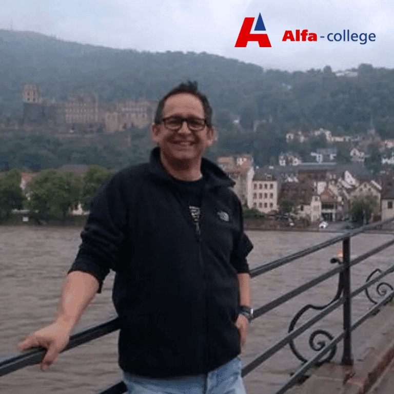 Portret van Bert Bennink van het Alfa-college, bij een waterkant, met op de achtergrond heuvels en het logo van Alfa-college in beeld