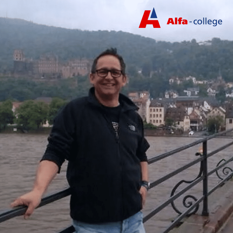 Portret van Bert Bennink van het Alfa-college, bij een waterkant, met op de achtergrond heuvels en het logo van Alfa-college in beeld